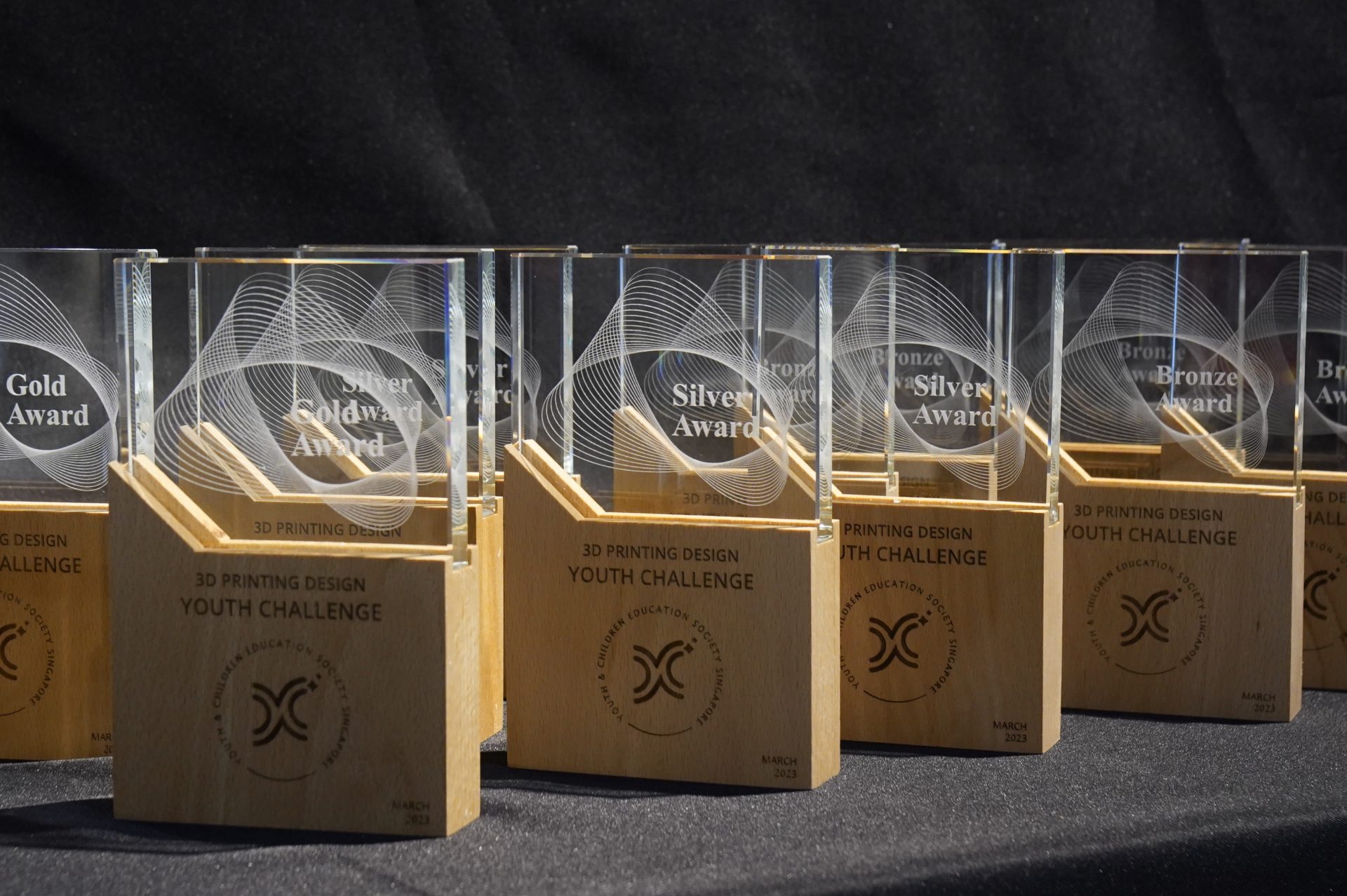 Gold, silver and bronze trophies lined up at the 3D Printing Design Youth Challenge